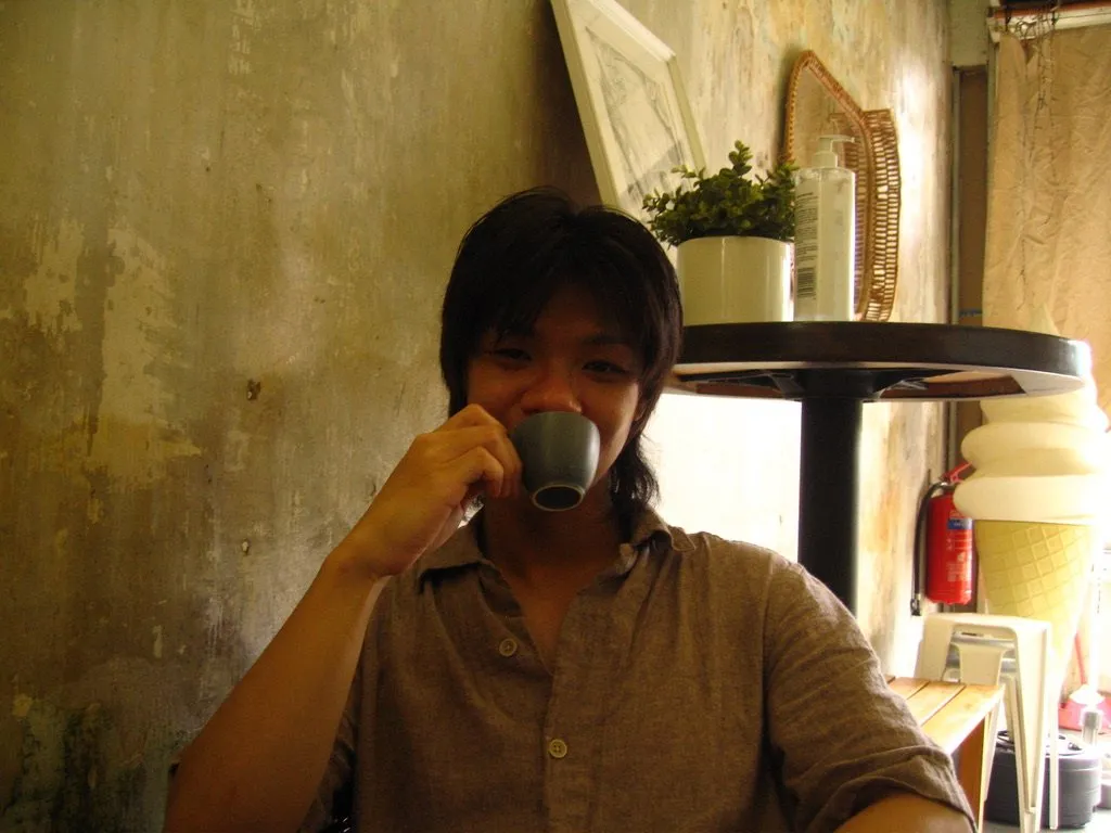 Drinking from a small cup in a cafe with a weathered wall behind.