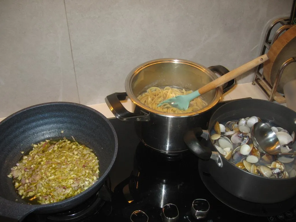 Linguine in a pot, clams in another, and garlic softening in a pan.