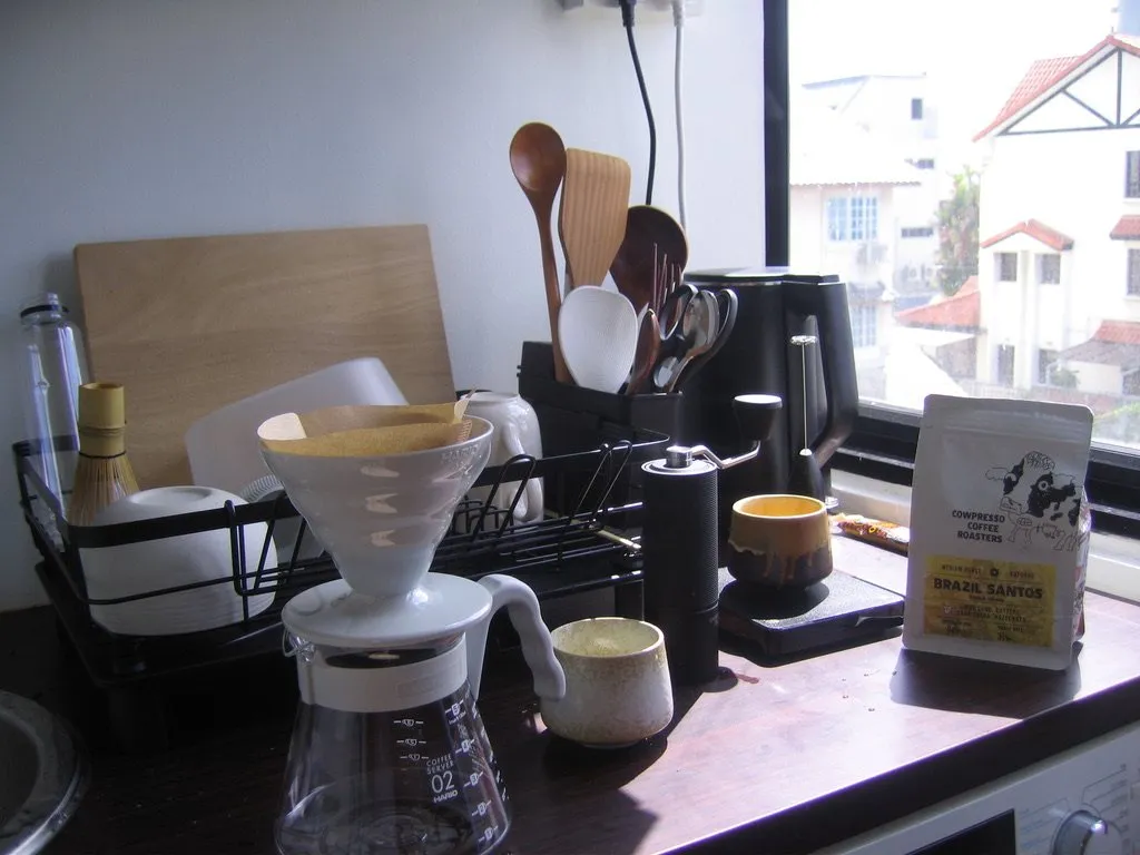 A V60 dripper, server and hand grinder on a kitchen bench by a window.