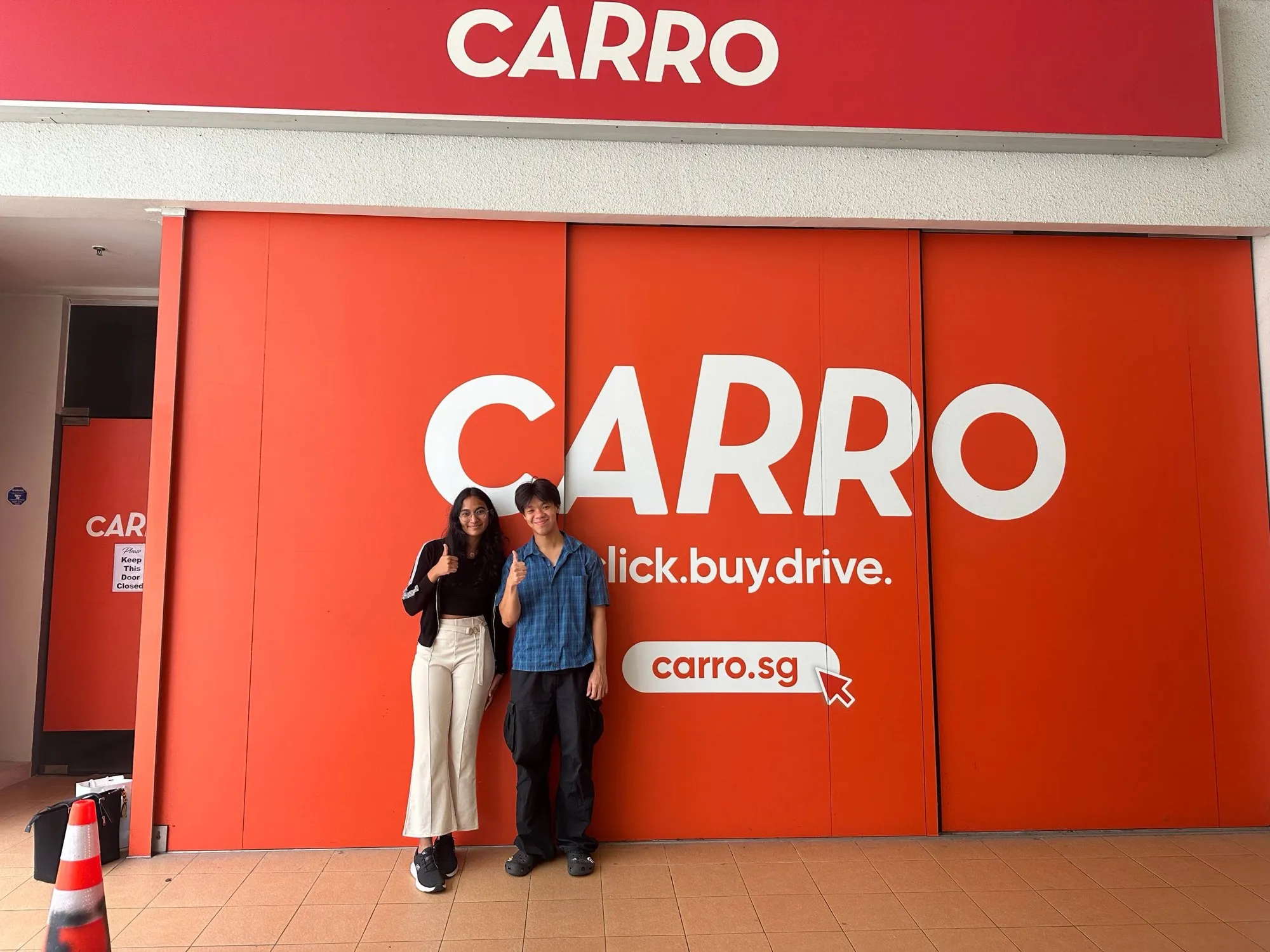 Zack and a colleague giving a thumbs up in front of the orange Carro wall at the Singapore office.