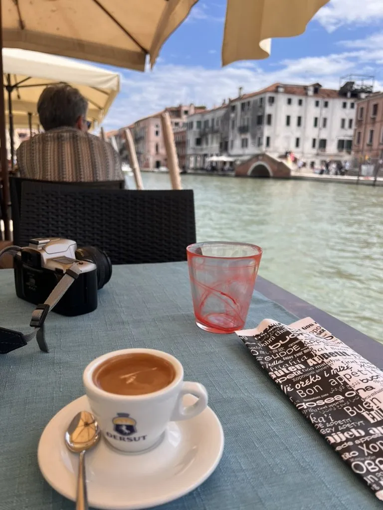 An espresso and a camera on a table beside a canal in Venice.